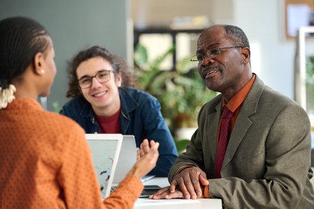 Portrait of smiling senior man discussing ideas in business meeting with young colleagues in office copy spaceの写真素材