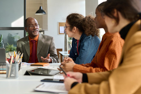 Diverse group of business people sitting at meeting table in office with senior African American man instructing employees copy spaceの写真素材