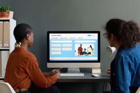Back view of two young business people using PC in office with focus on computer screen and job hunting website copy spaceの写真素材
