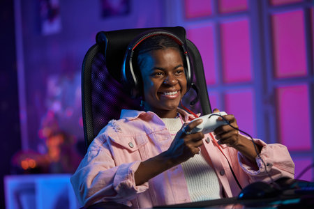 Portrait of smiling young African American woman playing video games and holding gamepad in studio...