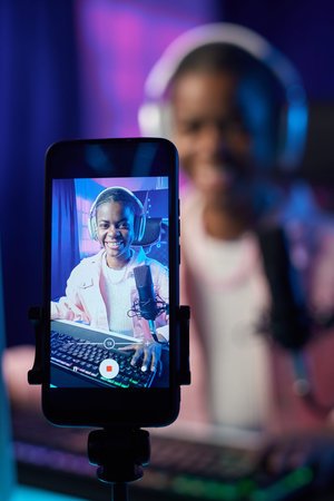 Vertical portrait of teenage girl playing video games and recording video with focus on smartphone...