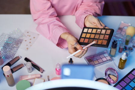 Top view closeup of young woman as beauty influencer recording makeup tutorial focus on hands holding palette with glittering eyeshadow copy spaceの写真素材