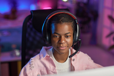 Front view portrait of young African American woman wearing headset while gaming in room with neon lights, copy spaceの写真素材
