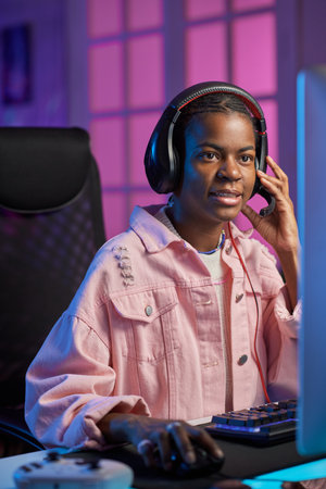 Vertical portrait of young Black girl wearing headset and playing videogames at nightの写真素材