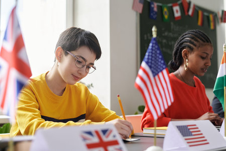 Portrait of young girl sitting at table with American flag during international conference in school classroom, copy spaceの写真素材