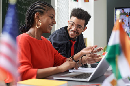 Side view portrait of two students man and woman laughing happily while enjoying work together in multicultural school classroomの写真素材