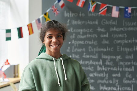Portrait of Black female student smiling at camera while standing by blackboard in classroom, copy spaceの写真素材