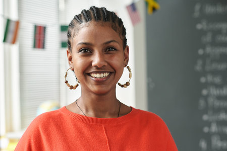 Portrait of young woman smiling at camera while standing by blackboard in school classroom, copy...