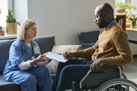 Side view portrait of African American man with disability signing medical form during at home doctors visit copy spaceの写真素材