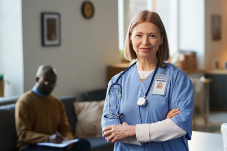 Waist up portrait of adult female doctor looking at camera standing with arms crossed in home setting with patient in background copy spaceの写真素材