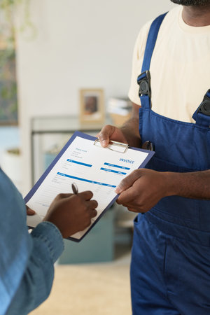 Vertical closeup of unrecognizable African American young woman signing service form with home maintenance worker holding clipboardの写真素材