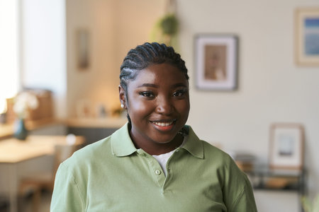 Front view portrait of young Black woman wearing uniform standing in home interior and smiling at...