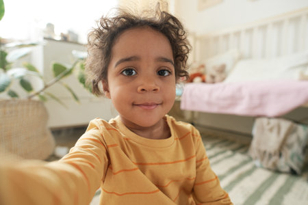 Portrait of smiling child in cozy bedroom with pastel decor, bed in background, potted plant partially visible in corner, capturing warm and inviting atmosphereの写真素材