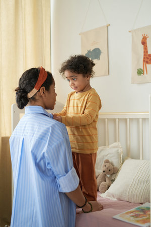 Mother engaging with her young child in dimly lit, cozy bedroom with animal posters on wall and bed...