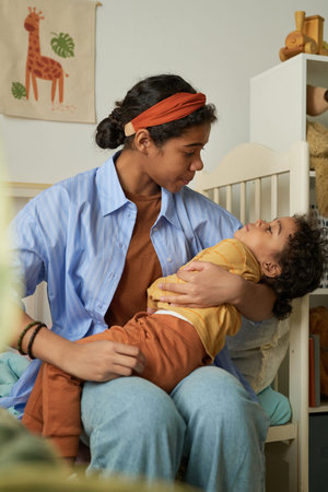 Mother holding her child in cozy bedroom, showing tender affection and nurturing care. Child looking...