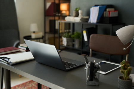 Modern home office setting with laptop on desk surrounded by books, notebooks, and shelves providing an organized and efficient workspaceの写真素材