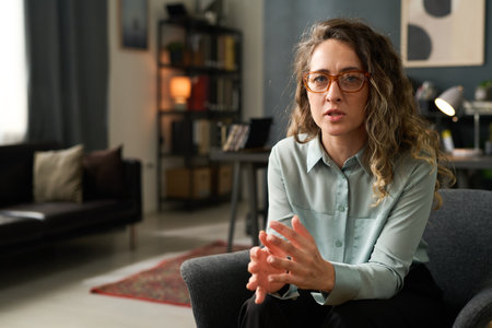 Portrait of woman wearing glasses while seated in modern living room with neutral-colored walls and shelves in background complementing cozy setupの写真素材