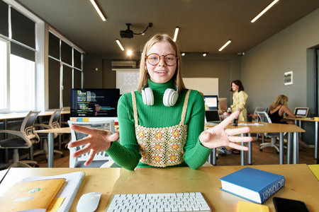 POV of young woman wearing glasses smiling at camera and gesturing while speaking via video chat in school classroomの写真素材
