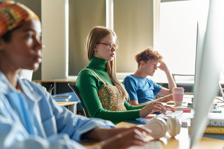 Group of young people sitting at desks with computers and examining programming code of software at class in schoolの写真素材