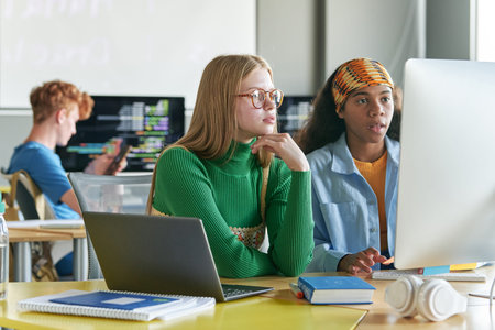 Girls sitting at desk with computers during IT class in school or college