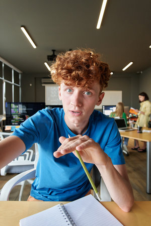Vertical portrait of young red haired man holding camera and talking to video chat POV