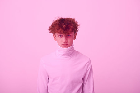 Portrait of a young man looking straight at camera, wearing high-neck sweater against pink...