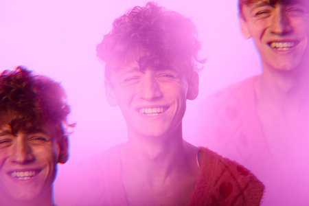 Portrait of cheerful young man smiling widely, surrounded by a warm pink glow creating an energetic...