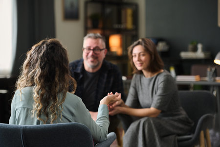 Back view of person consulting with smiling couple in cozy, warmly lit office with bookshelves in...