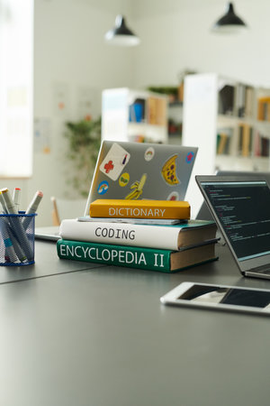 Vertical closeup of book stack on table in school library with laptop during programming class copy spaceの写真素材