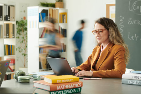 Side view portrait of smiling female teacher using computer in school library with children running...
