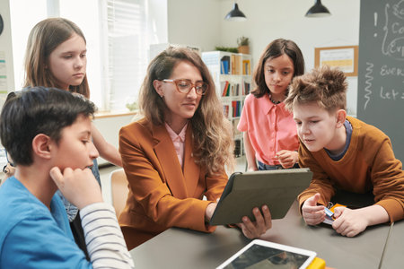 Portrait of smiling woman as female teacher using tablet with diverse group of young children in...