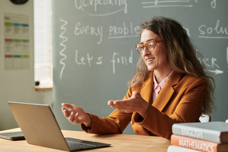 Side view portrait of smiling female teacher talking to video chat during online lesson with student and gesturingの写真素材