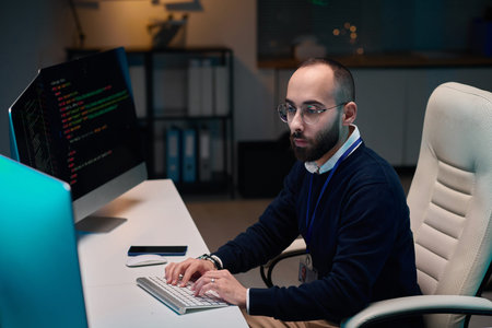 High angle portrait of bearded adult man using computer while coding while working late