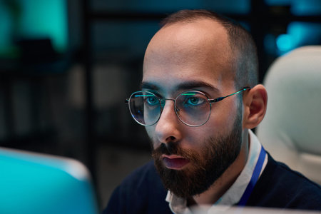 Minimal closeup of bearded adult man wearing glasses looking at computer screen while working late...