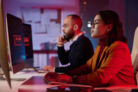 Side view portrait of computer programmers working in cybersecurity department with red emergency lights copy spaceの写真素材