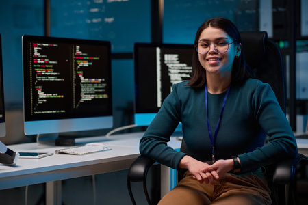 Portrait of smiling young woman wearing glasses as female computer programmer sitting at office workplace and looking at camera copy spaceの写真素材