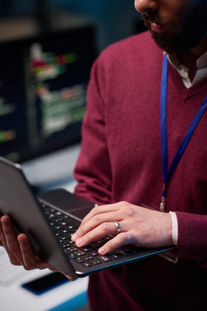 Vertical close up of unrecognizable man holding open laptop standing in IT development office with...