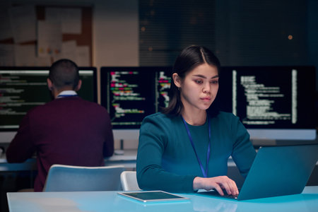Portrait of young woman as software development expert using laptop at minimal office workplace with blue neon light copy spaceの写真素材