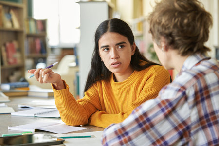 Female student explaining coursework concepts to another student in a library meeting room, with...