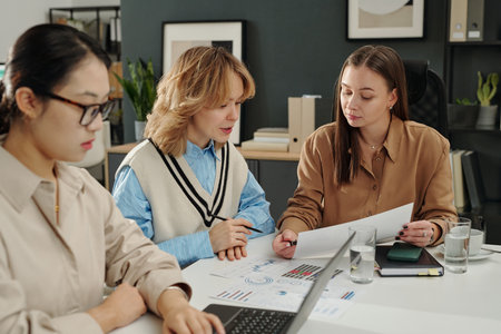 Candid shot of group of young women reading documents during work meeting in office and planning business strategyの写真素材