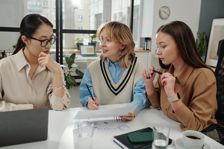 Front view portrait of all female team discussing document while working together during business meeting in officeの写真素材