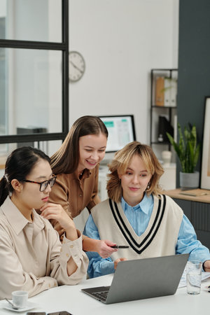 Vertical portrait of female manager pointing at laptop screen during work meeting with all girls business team in officeの写真素材