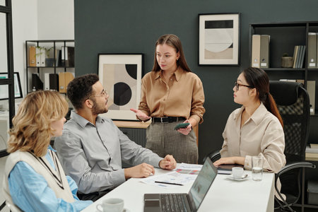Portrait of young businesswoman as female boss talking to team of colleagues while leading business meeting in officeの写真素材