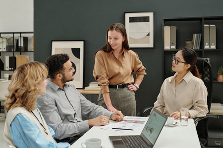 Portrait of smiling young businesswoman as female boss talking to team while standing by table at business meetingの写真素材