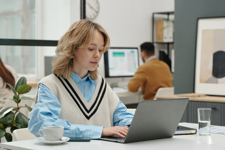 Portrait of gen Z young woman using laptop while sitting at workplace in modern office copy spaceの写真素材