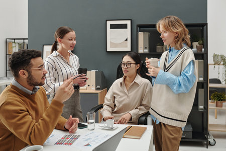 Young gen Z business team chatting cheerfully during coffee break in office holding coffee cups in meetingの写真素材