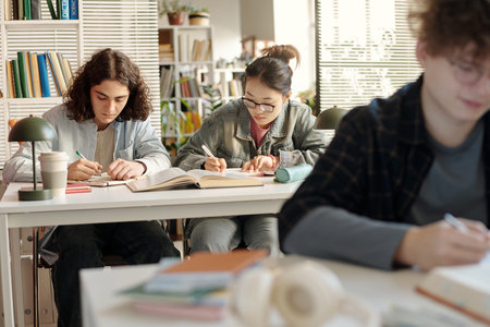 Over shoulder shot of two students sitting at desk in college classroom working together while...