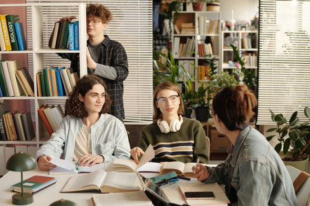 Candid shot of students studying together at table in college library and discussing school project while preparing for examsの写真素材