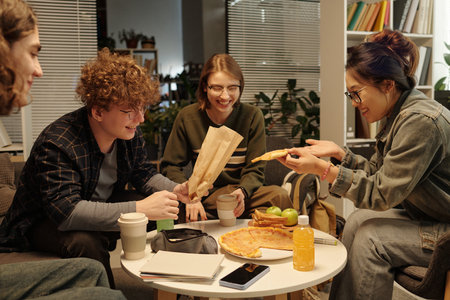 Group of students eating food and enjoying snacks while having fun together in lounge with low lightingの写真素材