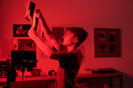 Creative side view shot of young photographer hanging freshly developed photo print for drying under...